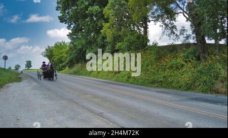 Ronks, Pennsylvania, 2021 giugno - Amish Open Horse and Buggy si avvicina con una coppia e una figlia in esso in una giornata di sole Foto Stock