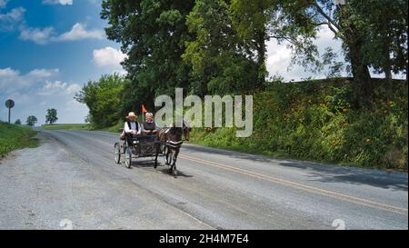 Ronks, Pennsylvania, 2021 giugno - Amish Open Horse and Buggy si avvicina con una coppia e una figlia in esso in un giorno di sole Foto Stock