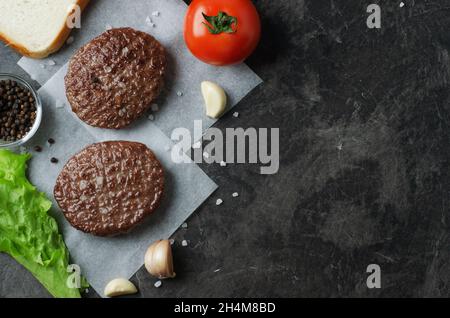 Ingredienti freschi fritti per hamburger di manzo con pomodori, insalate e aglio su sfondo scuro, vista dall'alto, spazio per il testo Foto Stock