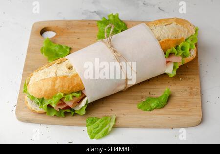 Sandwich di specialità gastronomiche con prosciutto, formaggio, pomodori e lattuga vista dall'alto sul tagliere Foto Stock