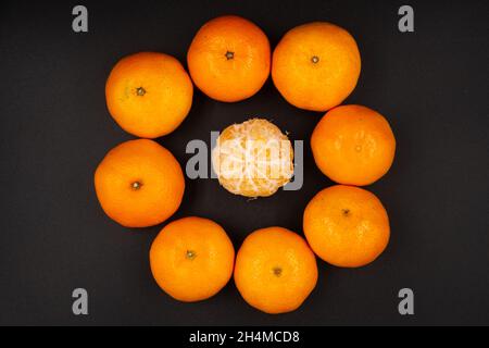 primo piano di mandarini arancioni maturi disposti in cerchio con un mandarino pelato al centro isolato su sfondo nero Foto Stock