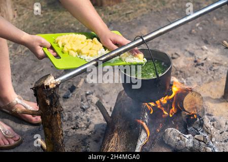 gettare gli ingredienti nella zuppa che viene cotta al fuoco in una pentola. Foto Stock