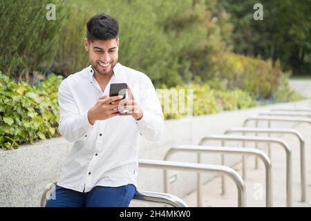 Bel giovane uomo misto da corsa, sorridente, con un cellulare all'aperto. Foto di alta qualità Foto Stock