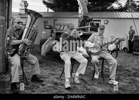 Un trio di musicisti suona sul lato della strada mentre si siede sugli sgabelli alla Deerfield Fair - Deerfield, New Hampshire. Ilford XP2 in bianco e nero Foto Stock