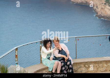 Due donne prendono selfie di fronte alle scogliere con il mare sotto Mirador es Colomer Mallorca Spagna Foto Stock