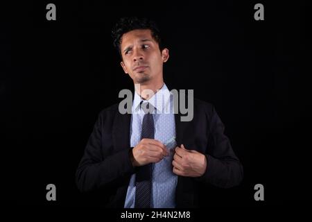 L'uomo d'affari corrotto riceve la tangente, isolato su sfondo nero. Uomo d'affari che mantiene i soldi nel suo vestito. Uomo sospettoso che nasconde denaro. Giovane latino Foto Stock