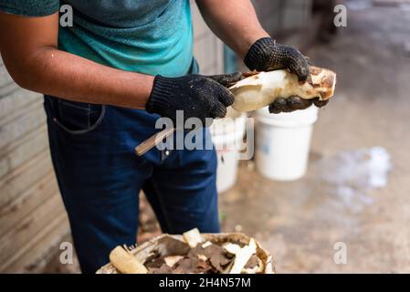 Uomo che indossa guanti neri peeling manioca per la cottura. Fiera di Sao Joaquim, Salvador, Bahia, Brasile. Foto Stock