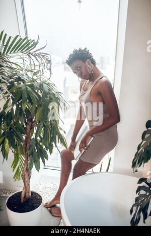 Donna giovane e accattivante con pelle scura in un vestito beige stretto Foto Stock