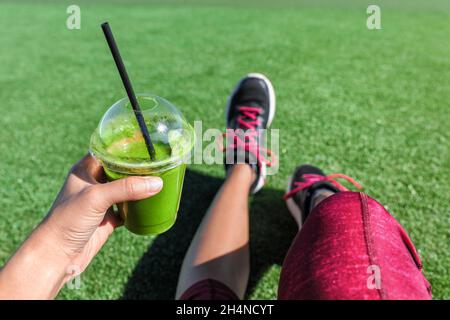 Green smoothie detox fitness ragazza bere tazza di plastica take-out mattina colazione succo durante la corsa nel parco estivo. Persona sportiva stile di vita sano POV Foto Stock