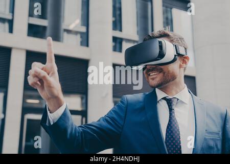 Uomo d'affari sorridente con occhiali per realtà virtuale che indossano stoppie, per vedere qualcosa in realtà virtuale Foto Stock