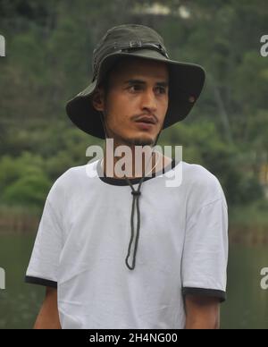 Girata in vita su di un ragazzo indiano bello osservare giovane in piedi all'aperto con il cappello di boonie e la maglietta bianca e guardando lateralmente Foto Stock