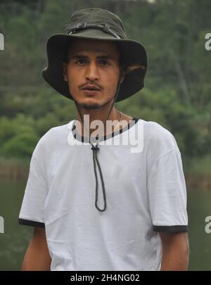 Girata in vita di un giovane indiano dall'aspetto bello in piedi all'aperto con cappello da boonie e maglietta bianca che guarda la macchina fotografica Foto Stock