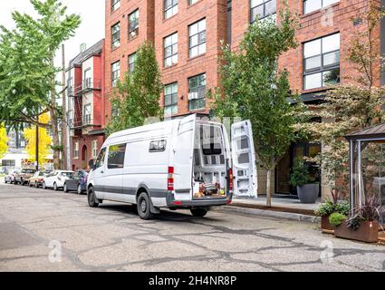 Commerciale carico compatto piccolo formato bianco mini furgone consegnato merci al cliente in multi-appartamento alto edificio e in piedi sulla strada autunno o Foto Stock