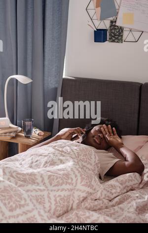 Donna africana stanca sdraiata nel letto e parlare al telefono cellulare nella sua camera da letto Foto Stock