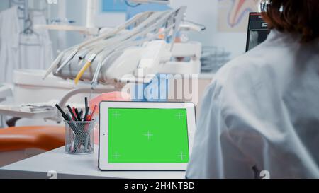 Primo piano di un tablet digitale con schermo verde orizzontale sulla scrivania nell'armadio odontoiatrico. Dentista che analizza il modello isolato e lo sfondo mockup con chiave cromatica per la cura stomatologica Foto Stock