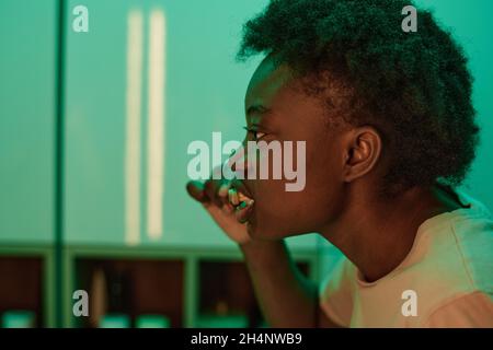 Primo piano della donna africana spazzolando i denti con lo spazzolino davanti allo specchio Foto Stock