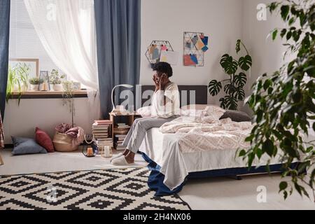 Giovane donna africana seduta sul letto con mal di testa, che ha un aspetto stanco e andare a letto Foto Stock