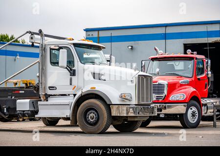 Due diversi semi-dumper Day Cab montati su pattini per il trasporto di contenitori per rifiuti sono parcheggiati l'uno vicino all'altro su un parcheggio del magazzino aw Foto Stock