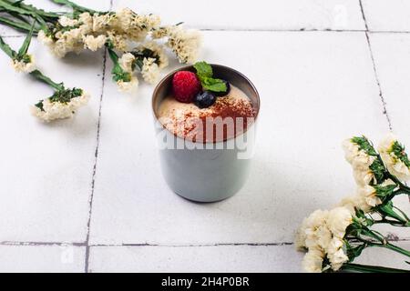 dessert al tiramisù in bicchiere con frutti di bosco su sfondo piastrellato bianco con fiori Foto Stock