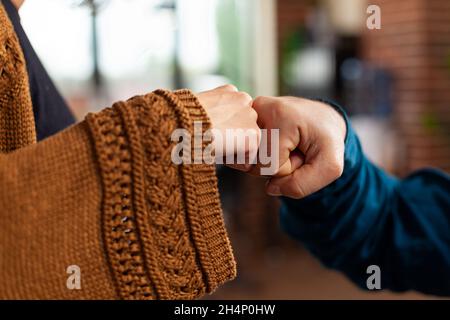 Primo piano di squadra con protezione medica maschera viso contro il cocid19 saluto dando primo urto in ufficio startup. Manager man seduto alla scrivania brainstorming idee per la strategia di definizione dei progetti aziendali Foto Stock