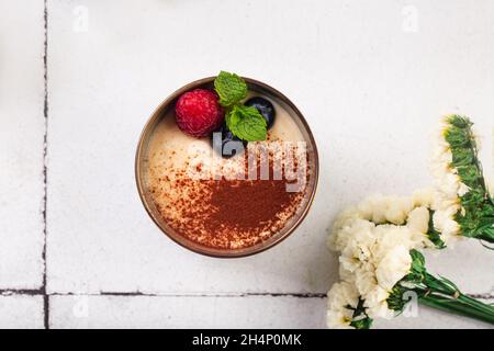 dessert al tiramisù in bicchiere con frutti di bosco su sfondo piastrellato bianco con fiori Foto Stock