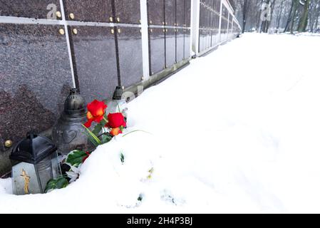 fiori e candele di fronte al muro di colombario in cimitero nella neve in inverno Foto Stock