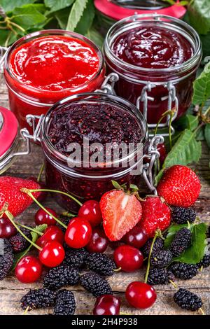 confettura di fragole, ciliegie e gelsi su un tavolo rustico Foto Stock