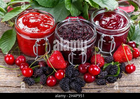 confettura di fragole, ciliegie e gelsi su un tavolo rustico Foto Stock