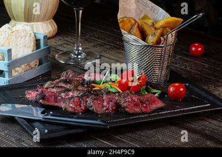Bistecca di manzo alla griglia tagliata a fette con patate al forno servita su un piatto quadrato. Foto Stock