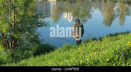 Un pescatore cattura il pesce, si trova accanto al lago. Estate, tempo soleggiato, lago con riflessi d'acqua. Foto Stock