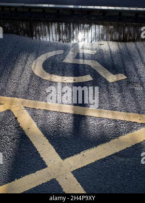 Qui vediamo i modelli di ombre fuse da una recinzione, ponte ferroviario e cartelli su uno spazio di parcheggio per disabili nel parcheggio della stazione di Radley. È la pandemia, s Foto Stock