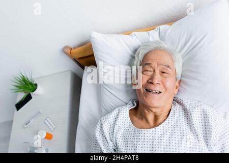 Vista dall'alto di un paziente asiatico allegro che si trova sul letto del reparto ospedaliero Foto Stock