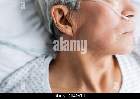 Vista ritagliata del paziente anziano con cannula nasale appoggiata sul letto dell'ospedale Foto Stock