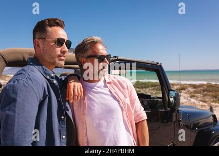 Felice coppia maschio gay caucasico abbracciando da una macchina al mare Foto Stock