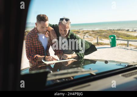 Felice coppia caucasica gay maschio lettura mappa appoggiarsi sul cofano di auto al mare Foto Stock