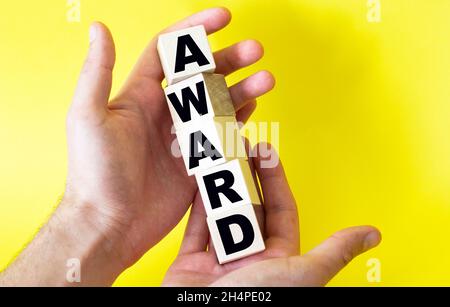 Mani che tengono blocchi di legno con testo premio su uno sfondo giallo Foto Stock