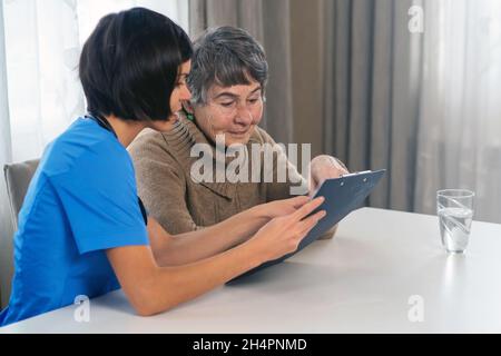 Giovane infermiera si prende cura di una donna anziana di 80 anni a casa Foto Stock
