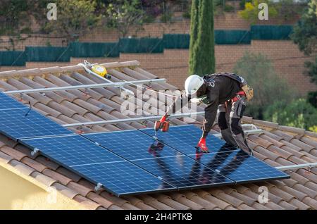 I lavoratori con contratto elettrico per HolaLuz installano pannelli solari sul tetto di una casa residenziale durante la messa a punto di un impianto elettrico sovvenzionato per abitazioni private, a nord di Barcellona, a Carbils, Catalogna, Spagna. © Olli Geibel Foto Stock