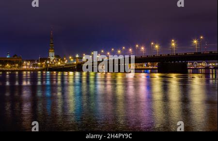 Vista notturna del centro storico della città e del ponte di pietra dalle rive del fiume Daugava colorato con luci di strada, riga, Lettonia Foto Stock