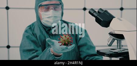 Medico con un modello di coronavirus in mano in un ufficio medico con un microscopio Foto Stock