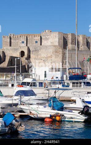 Alcune delle piccole barche nel porto di Puerto de Tarifa, Andalucía, Spagna meridionale, con il Castillo de Guzman el Bueno (castello costruito nel 960) Foto Stock