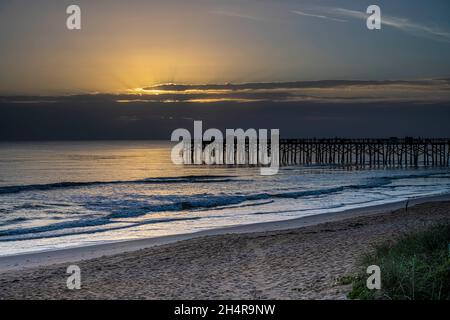 Raggi di sole che si infrangono attraverso le nuvole di tempesta scura all'orizzonte sopra il molo di pesca di Flagler Beach in Florida. Foto Stock