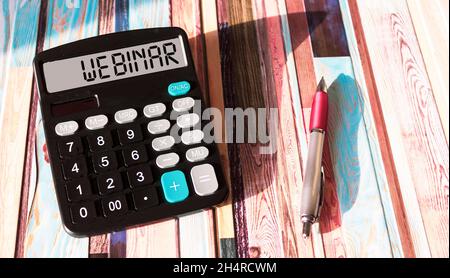 La parola WEBINAR è scritta sul display della calcolatrice. Concetto di business e finanza. Una penna su uno sfondo colorato. Foto Stock