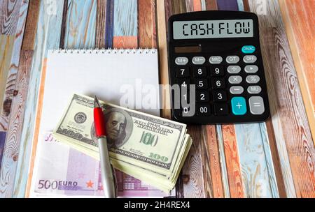 La parola flusso di cassa su una calcolatrice ulteriormente primo piano con dollari ed euro, un blocco note e una penna Foto Stock
