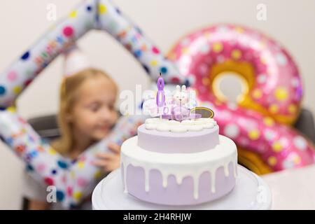 Felice piccola ragazza caucasica con emozione positiva sul volto festeggiando il compleanno di otto anni a casa. Candido lifestyle ritratto di Kid soffiando Foto Stock