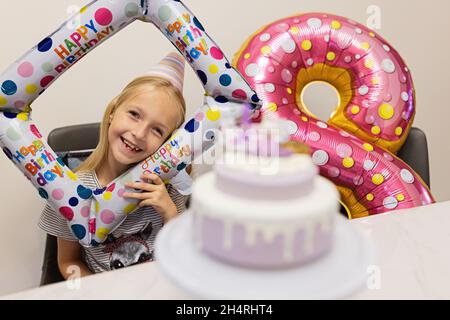 Felice piccola ragazza caucasica con emozione positiva sul volto festeggiando il compleanno di otto anni a casa. Candido lifestyle ritratto di Kid soffiando Foto Stock