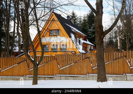 Zakopane, Polonia - 21 marzo 2018: L'edificio in legno nascosto dietro la recinzione in legno è coperto da un tetto ripido. Intorno ci sono alcuni alberi withou Foto Stock