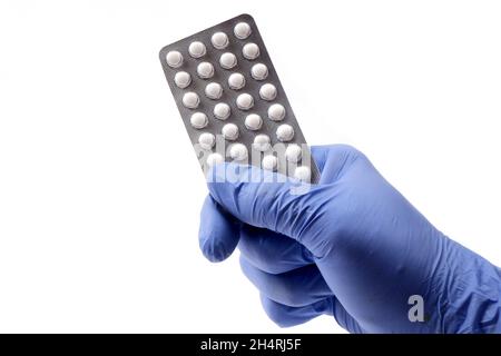 un blister di pillole è tenuto da una mano del medico in guanti blu monouso. Foto Stock
