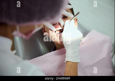 vista del ragazzo della scuola su appuntamento dentale. Primo piano della cavità orale del ragazzo seduto sulla sedia dentale mentre il dentista pediatrico esamina la tettarella Foto Stock