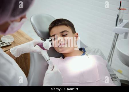 Adorabile bel bambino, ragazzo di scuola seduto in sedia del dentista durante la visita pediatrica dentista in clinica dentale bianca moderna, ricevendo medico orale c Foto Stock